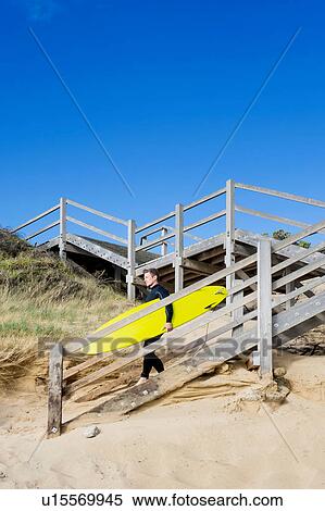 Stock Photography - Surfer carrying surf board descending to beach. Fotosearch