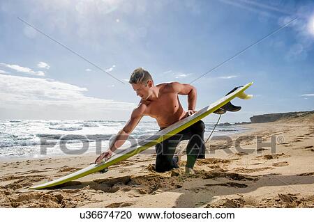 Stock Image - Surfer preparing surf board on beach. Fotosearch