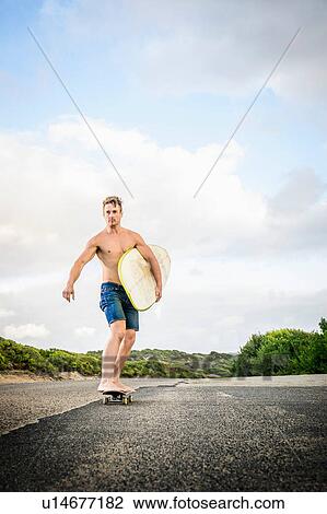 Stock Image - Surfer skateboarding with surfboard under arms. Fotosearch