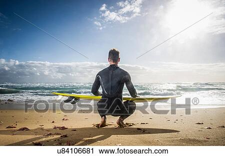 Stock Image - Surfer squatting with surf board. Fotosearch