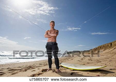 Surfer standing beside surf board with arms crossed View Large Photo Image Stock Photo - Surfer standing beside surf board with arms crossed. Fotosearch