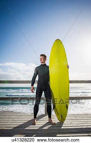 Surfer standing holding surfboard View Large Photo Image Stock Image - Surfer standing holding surfboard. Fotosearch