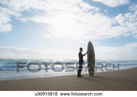 Surfer standing holding surfboard View Large Photo Image Stock Photo - Surfer standing holding surfboard. Fotosearch