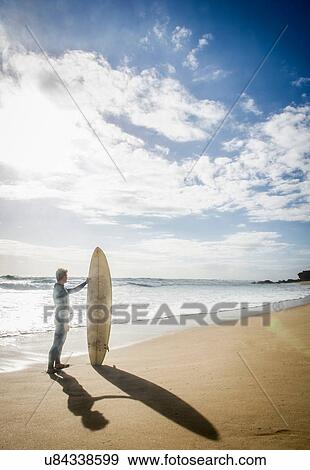 Surfer standing holding surfboard View Large Photo Image Stock Photo - Surfer standing holding surfboard. Fotosearch