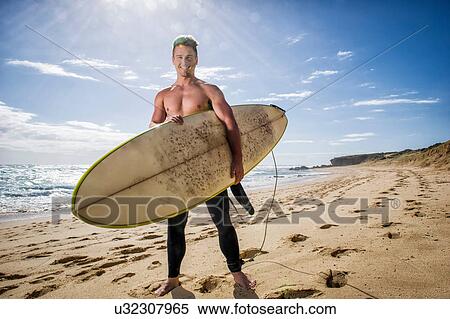 Stock Photography - Surfer standing holding surfboard. Fotosearch