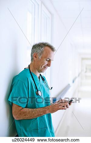 Surgeon standing in corridor looking at smartphone View Large Photo Image Stock Photo - Surgeon standing in corridor looking at smartphone. Fotosearch