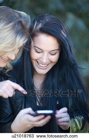 Two young females looking at mobile View Large Photo Image Stock Image - Two young females looking at mobile. Fotosearch