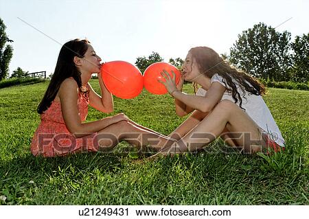 Two young women sitting on grass bowing up red balloons View Large Photo Image Stock Image - Two young women sitting on grass bowing up red balloons. Fotosearch