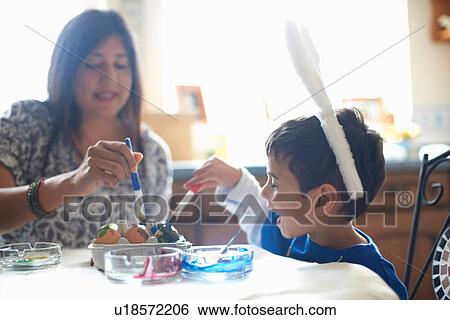 Stock Photograph - Woman and boy wearing bunny ears painting Easter eggs. Fotosearch