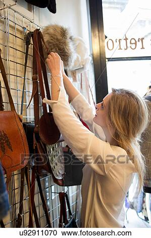 Stock Image - Woman hanging up bags in vintage clothes shop. Fotosearch