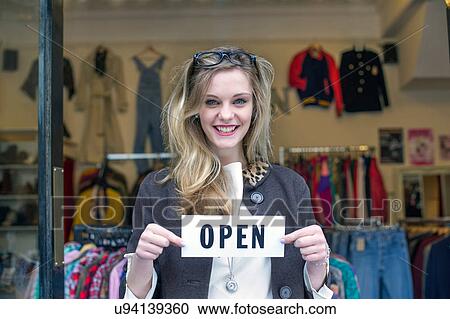Stock Image - Woman holding open sign in clothes shop. Fotosearch