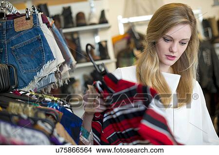 Picture - Woman looking at top garment. Fotosearch