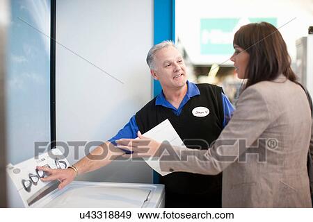 Stock Photo - Woman looking at washing machine in showroom. Fotosearch