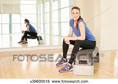 Stock Photo - Woman sitting on step in gym. Fotosearch