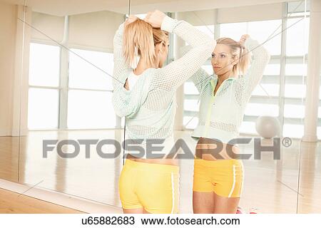 Stock Image - Women doing her hair in mirror in gymnasium. Fotosearch