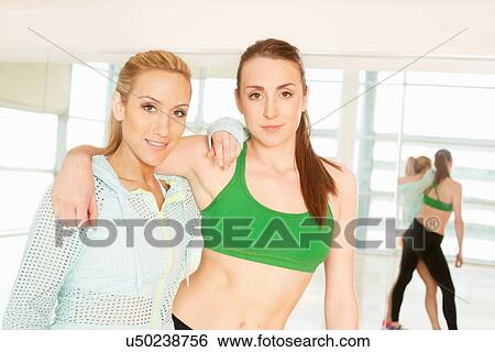 Stock Photograph - Women standing in gymnasium with arm around. Fotosearch