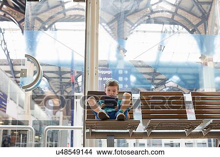 Young boy in train station waiting room playing handheld game View Large Photo Image Picture - Young boy in train station waiting room playing handheld game. Fotosearch