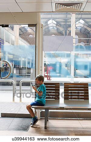 Young boy in train station waiting room playing electronic game View Large Photo Image Stock Image - Young boy in train station waiting room playing electronic game. Fotosearch