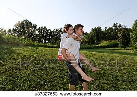 Stock Image - Young man giving piggyback ride to young woman. Fotosearch