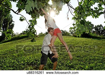 Stock Image - Young man lifting young woman to tree branches. Fotosearch