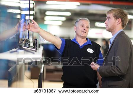 Stock Photo - Young man looking at flat screen TV in showroom. Fotosearch