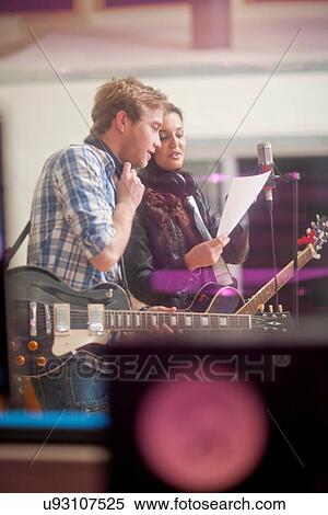 Stock Photography - Young musicians looking at sheet of paper in recoding studio. Fotosearch