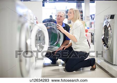 Stock Image - Young woman and salesman looking at washing machines in showroom. Fotosearch
