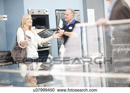 Young woman and salesman looking at ovens in showroom View Large Photo Image Stock Image - Young woman and salesman looking at ovens in showroom. Fotosearch