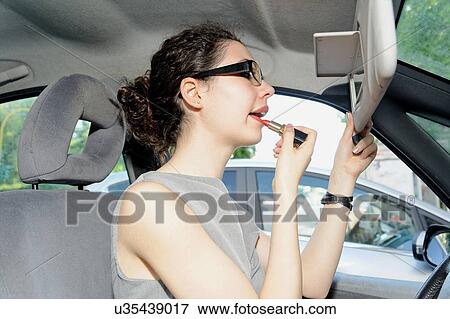 Young woman applying lipstick in car View Large Photo Image Stock Photo - Young woman applying lipstick in car. Fotosearch