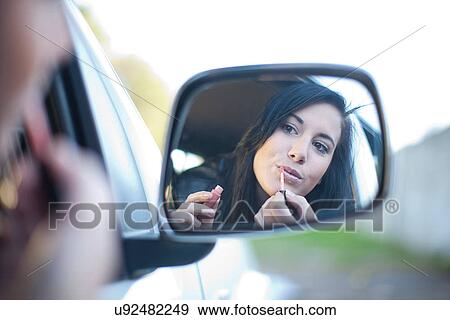 Young woman applying lipstick in car mirror View Large Photo Image Stock Photo - Young woman applying lipstick in car mirror. Fotosearch