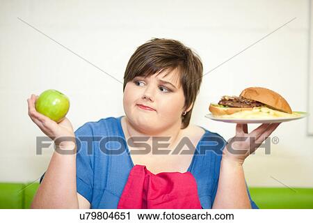 Young woman choosing between an apple and a burger View Large Photo Image Stock Image - Young woman choosing between an apple and a burger. Fotosearch