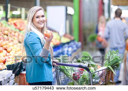 Young woman holding apple in indoor market View Large Photo Image Stock Image - Young woman holding apple in indoor market. Fotosearch