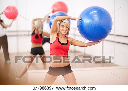Stock Photo - Young woman holding exercise ball in aerobics class. Fotosearch