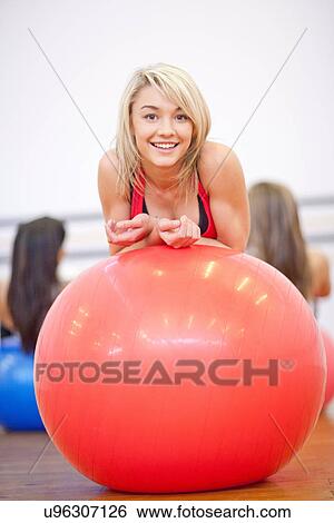 Stock Photograph - Young woman resting on exercise ball in aerobics class. Fotosearch