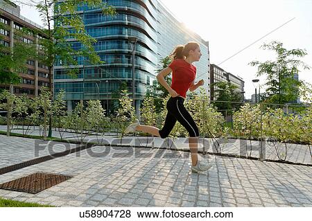 Stock Photo - Young woman running past office buildings. Fotosearch