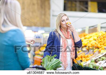 Stock Photo - Young women buying produce in indoor market. Fotosearch