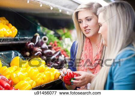Stock Photo - Young women looking at peppers in supermarket. Fotosearch