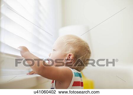 Stock Image - Baby boy (6-11 months) looking through window. Fotosearch