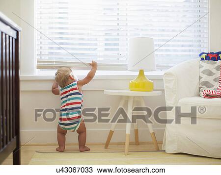 Stock Image - Baby boy (6-11 months) looking through window. Fotosearch