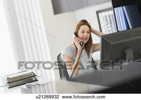 Stock Image - Business woman using computer and phone in office. Fotosearch