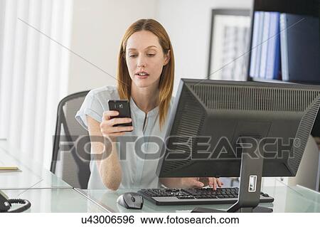 Stock Photograph - Business woman using computer and phone in office. Fotosearch