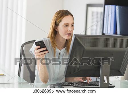 Stock Photography - Business woman using computer and phone in office. Fotosearch