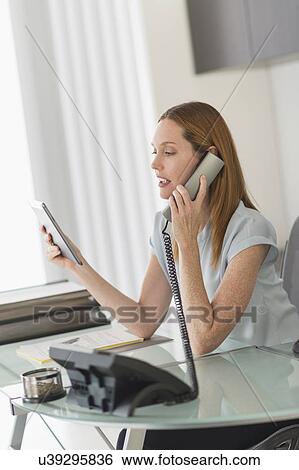 Stock Photograph - Business woman using phone and tablet pc in office. Fotosearch