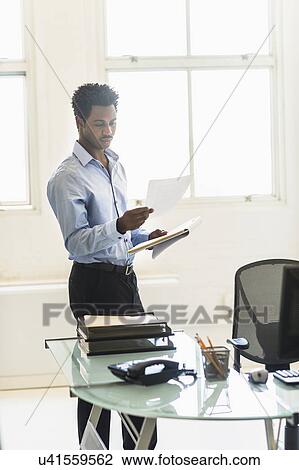 Businessman reading documents in office View Large Photo Image Stock Image - Businessman reading documents in office. Fotosearch