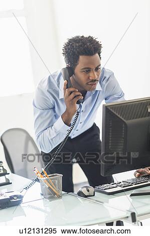 Businessman working on computer and talking on cell phone View Large Photo Image Stock Photography - Businessman working on computer and talking on cell phone. Fotosearch
