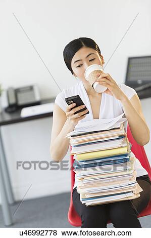 Stock Photo - Businesswoman with stack of files texting on phone. Fotosearch