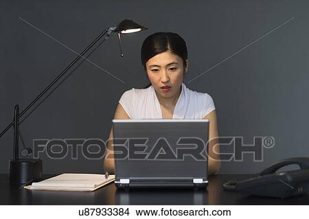 Picture - Businesswoman working on laptop at night. Fotosearch