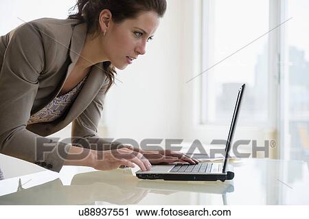 Stock Image - Busy woman in office using laptop. Fotosearch