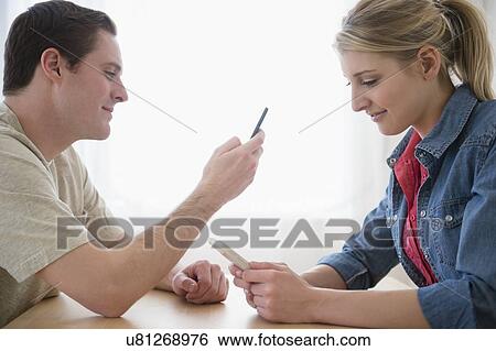 Stock Photograph - Couple at table using smartphones. Fotosearch