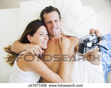 Couple lying on bed photographing themselves View Large Photo Image Stock Photo - Couple lying on bed photographing themselves. Fotosearch